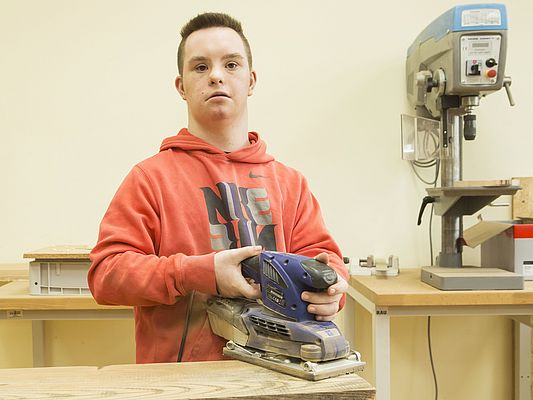 Mit einer Schleifmaschine beseitigt Schüler Joey die Unebenheiten im Holz, das anschließend zu Intelligenzspielzeug weiterverarbeitet wird
